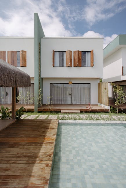 An aerial view of a residential neighborhood featuring a series of terraced houses with small, well-maintained gardens. The gardens display a variety of textures including neatly trimmed grass lawns,